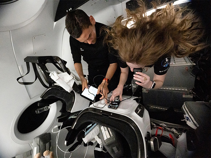 Two people in zero gravity monitor the scientific equipment